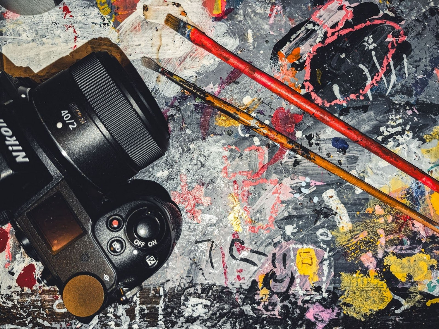 Image showing a DSLR, paint brushes, and a painted canvas underneath to give a visual of Modern art by Joe Papagoda