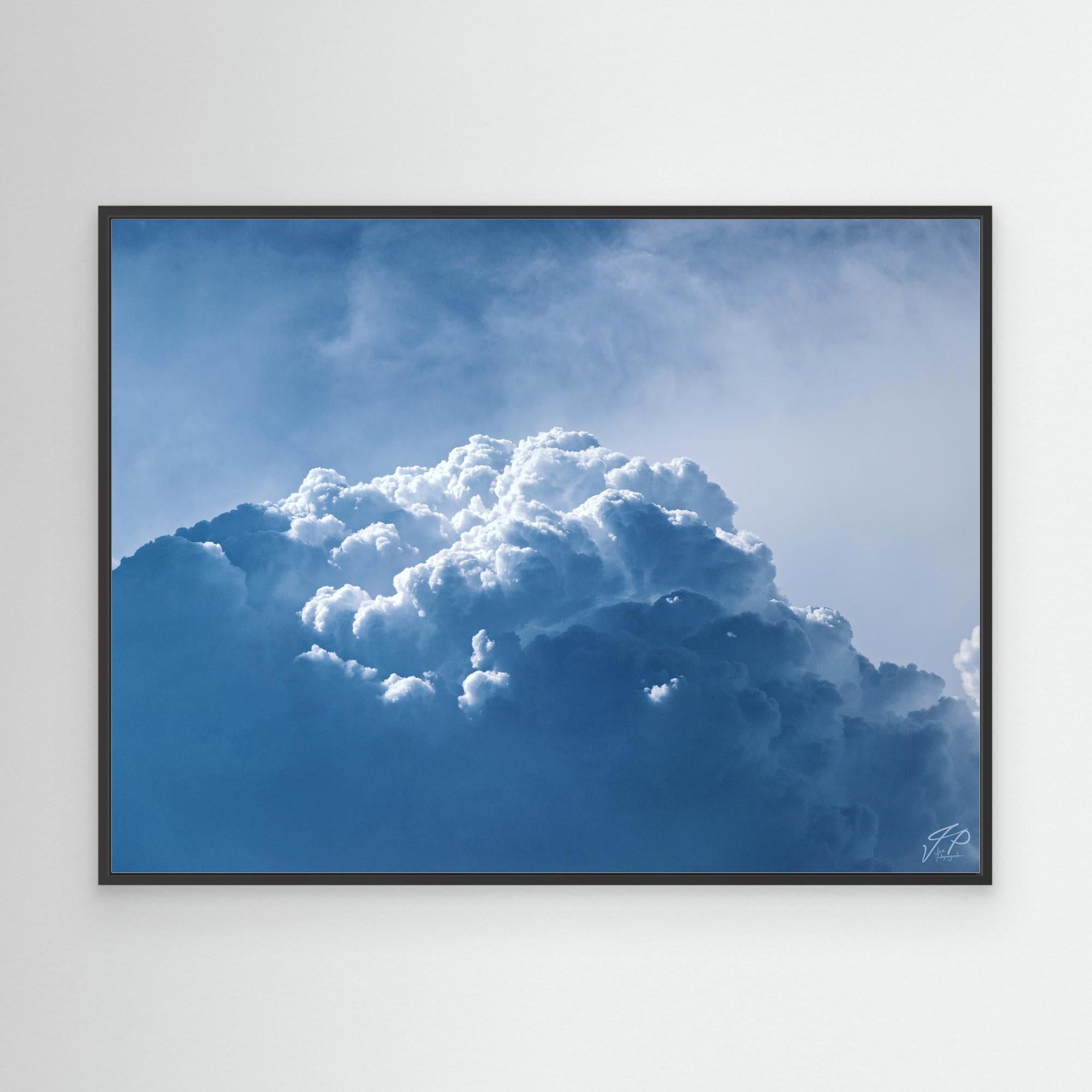 Framed photograph of a large cloud against a blue sky on a white wall.
