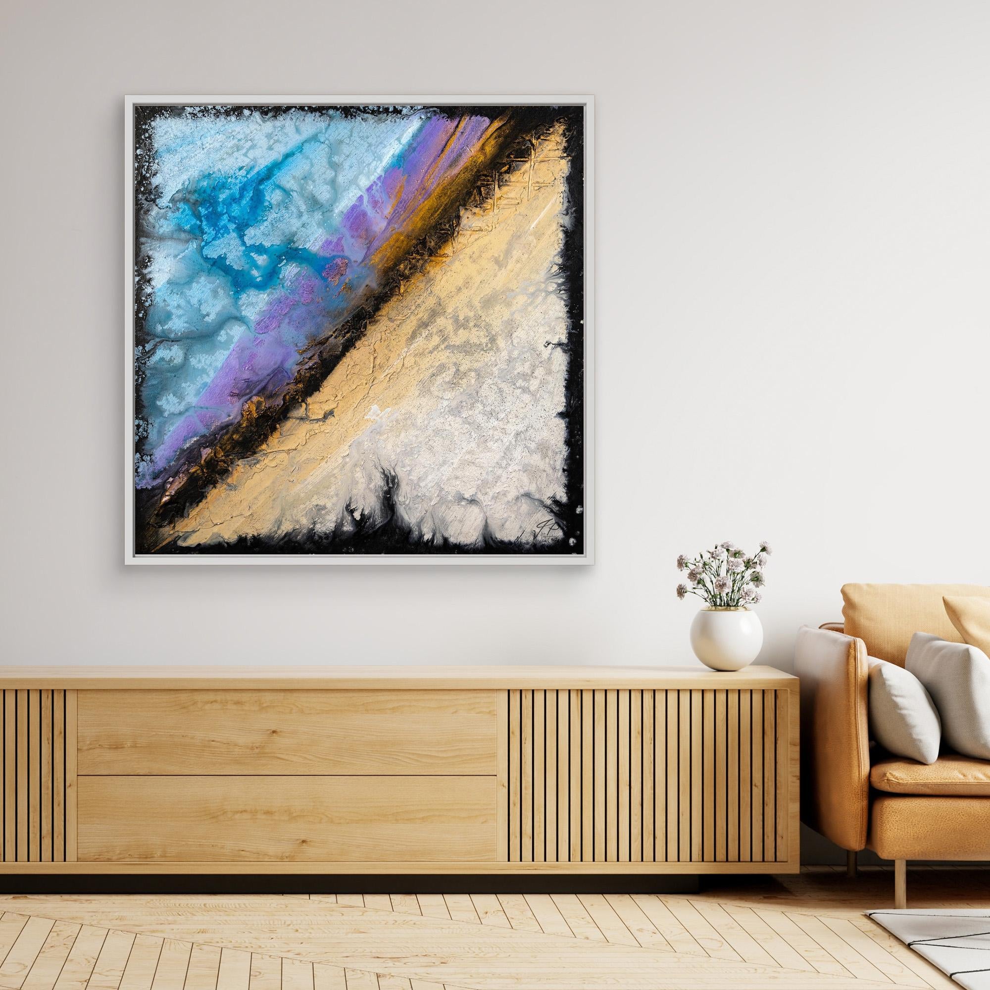 Framed abstract art with blue, purple, beige, and gold textures above a wooden console next to an armchair.