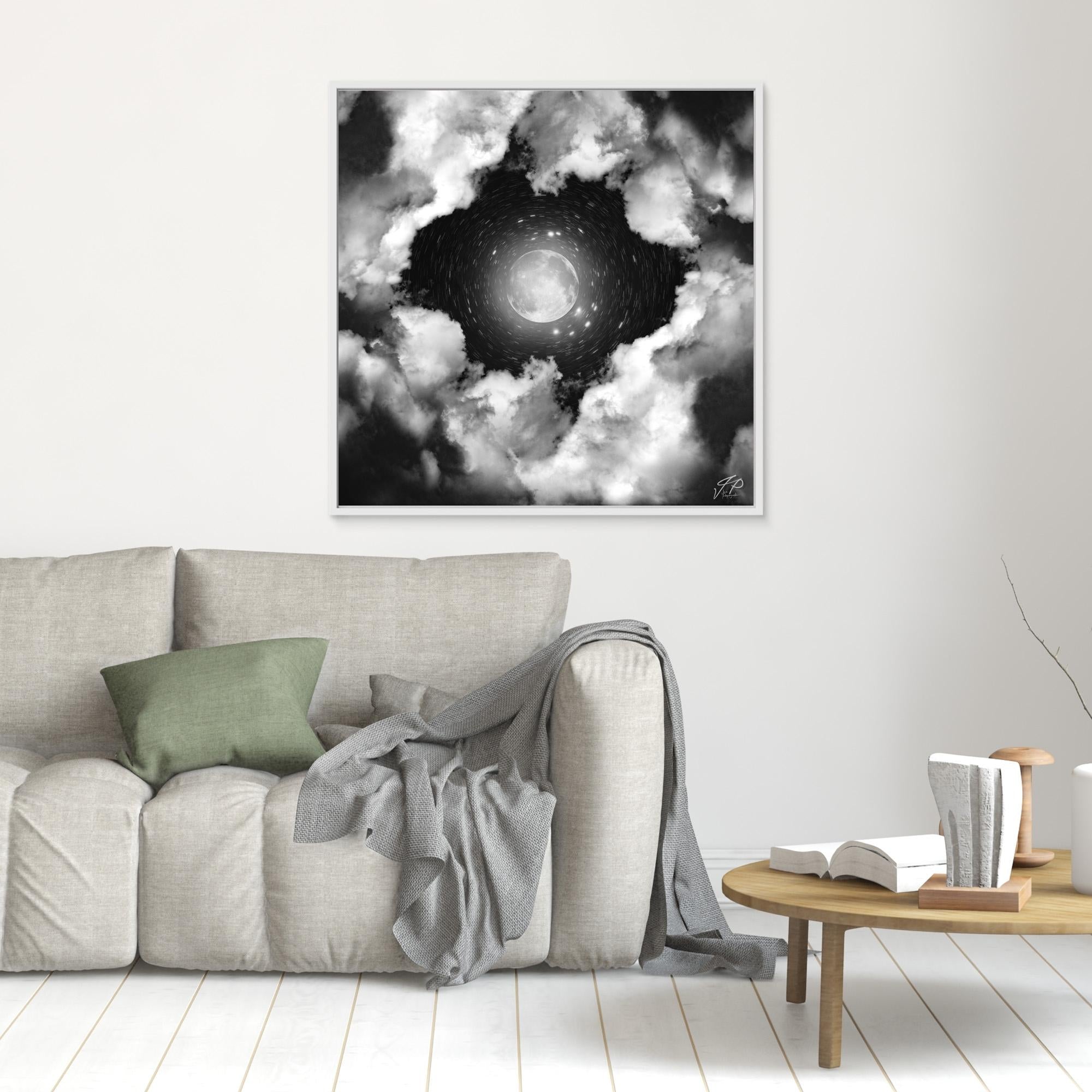 Monochrome moon and swirling clouds art above a light sofa and small round side table.