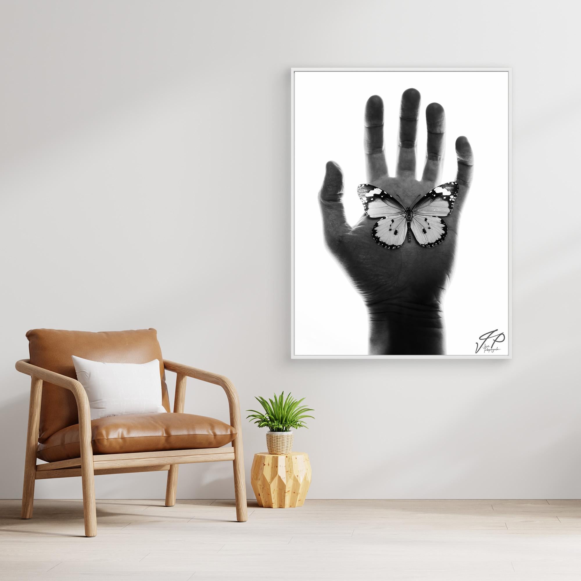 Minimalist room with tan leather chair, small plant, and black-and-white artwork of a hand with a butterfly.