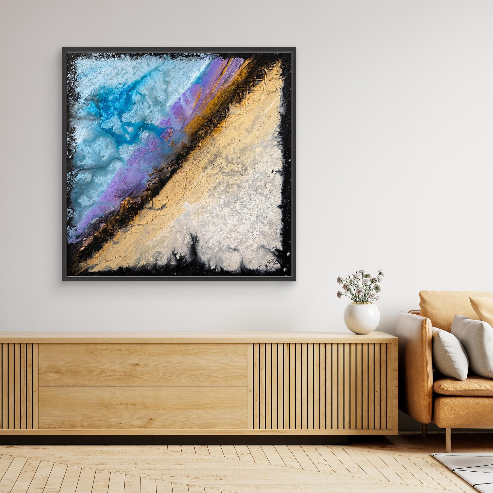 Framed abstract art with blue, purple, beige, and gold textures above a wooden console next to an armchair.