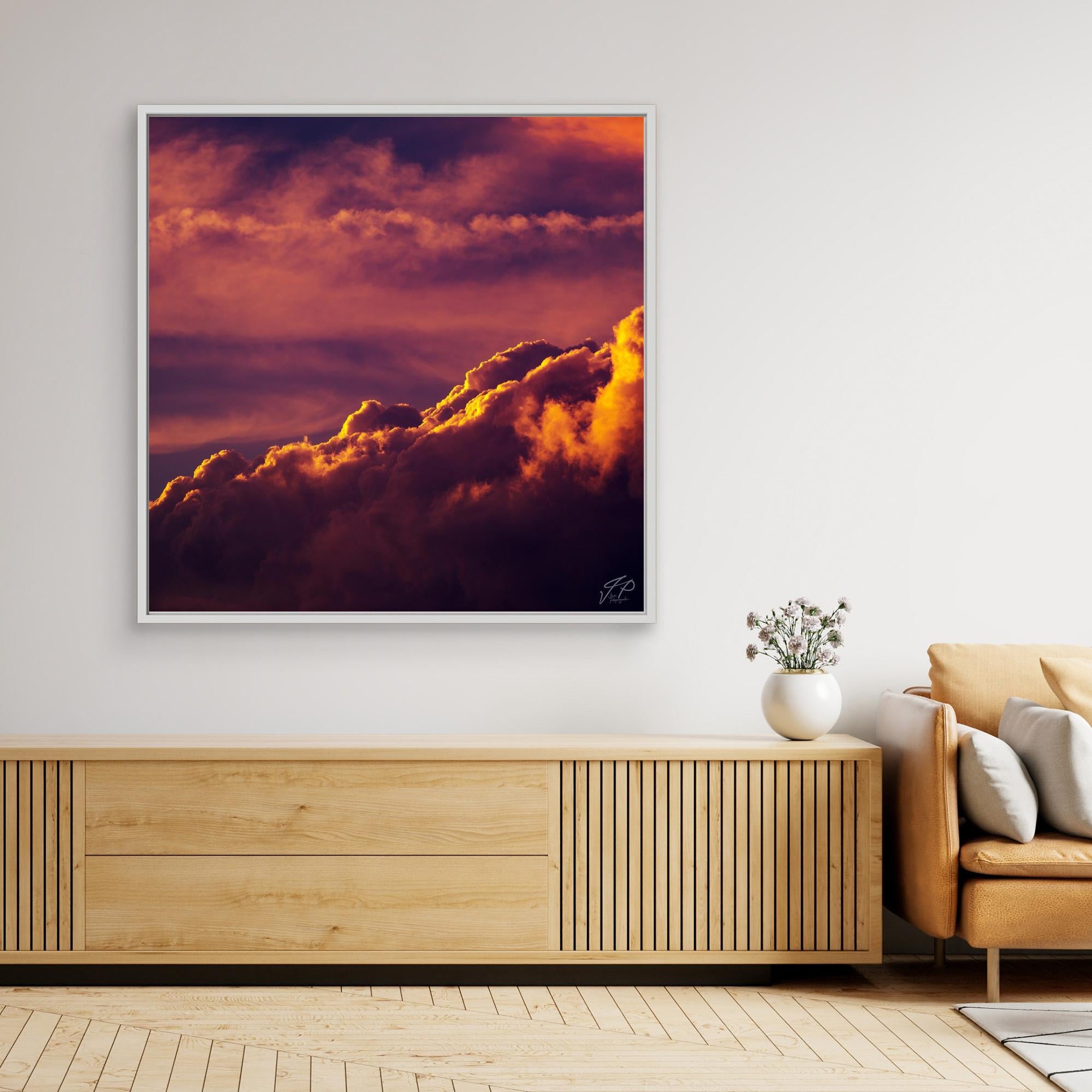 A vivid sunset clouds photograph in a white frame hangs above a wooden console and beige armchair.