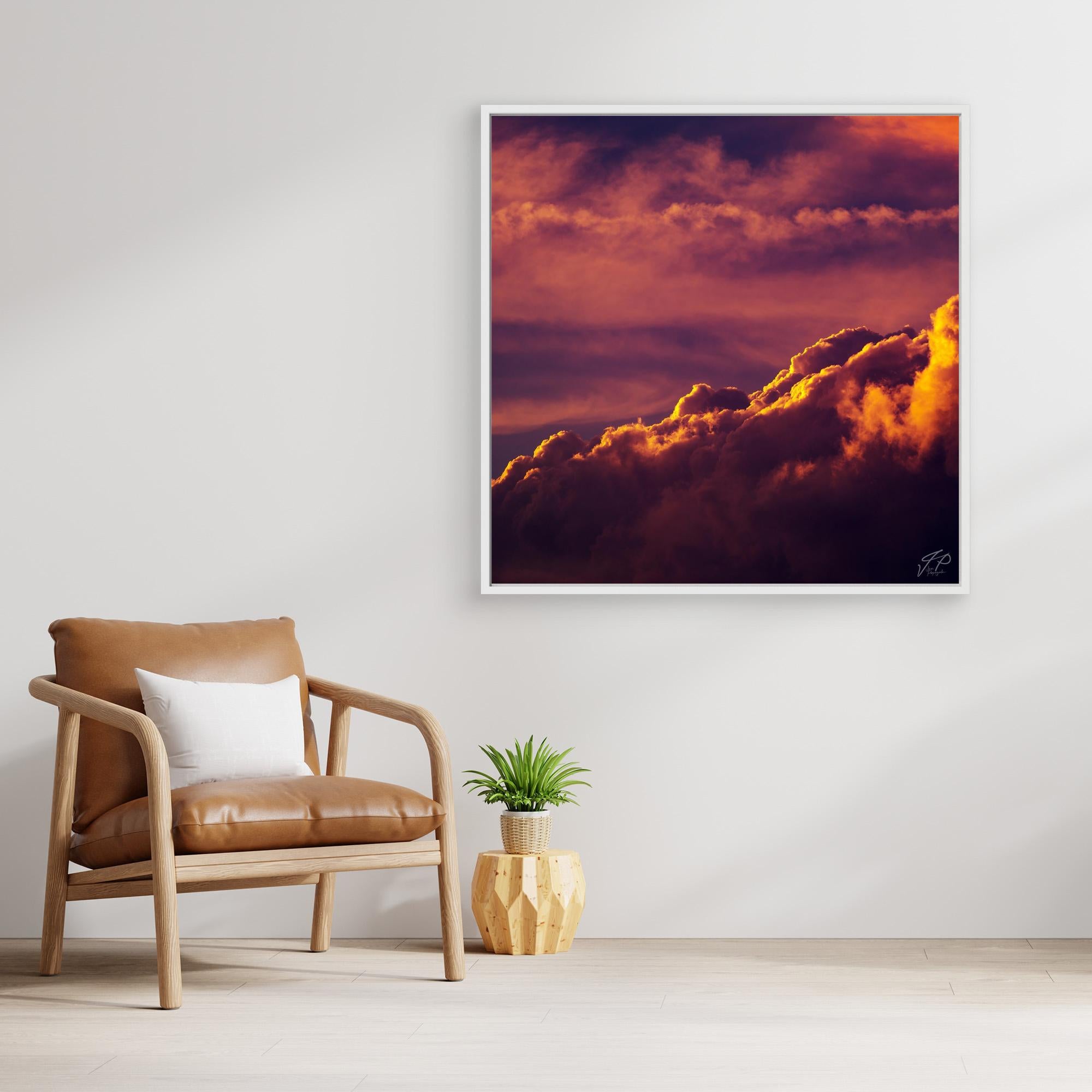Sunset cloud photograph with orange and purple tones hangs above a tan chair and geometric plant stand.