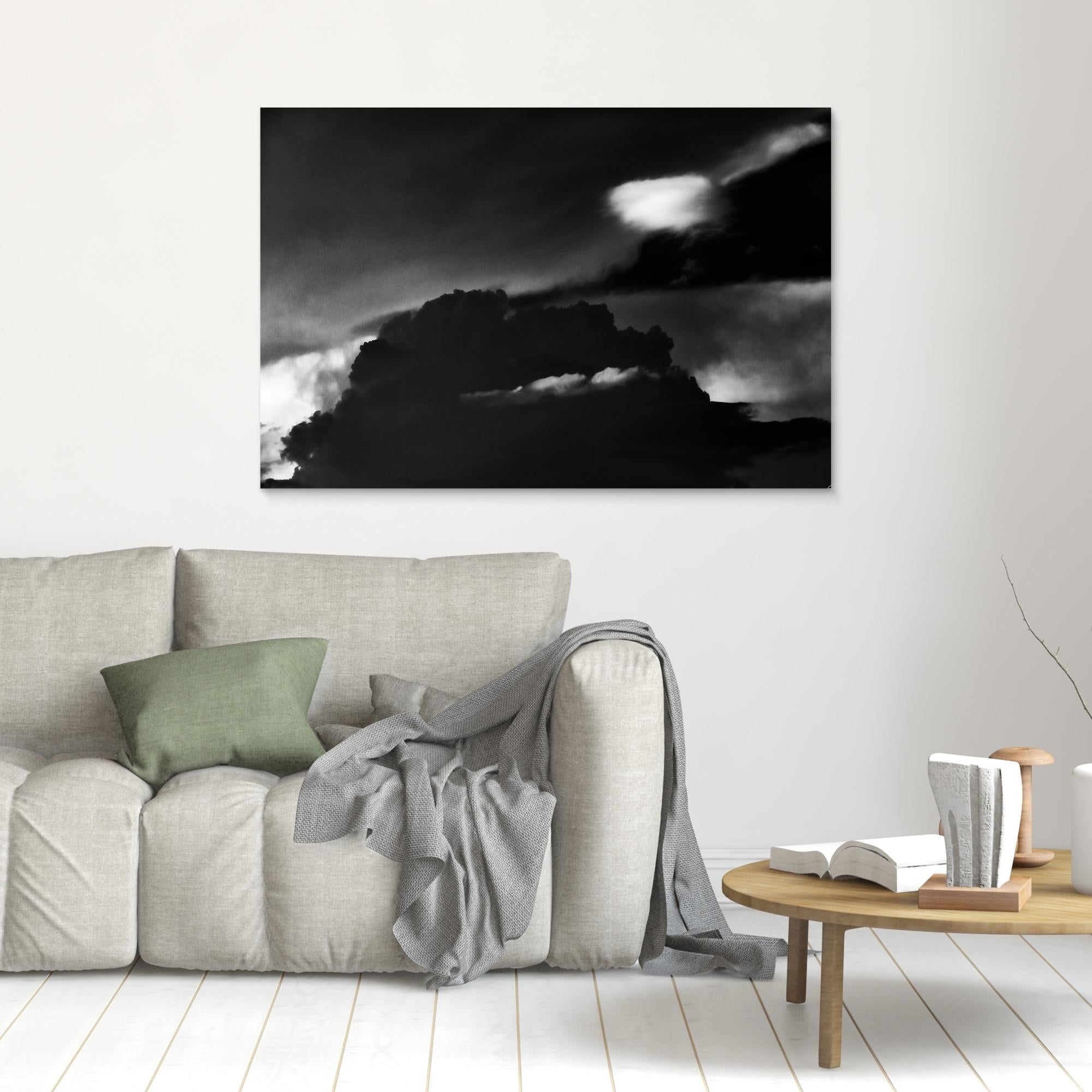 Living room with a gray sofa, green pillow, and wooden coffee table with a book and vase. A large black and white cloud painting is on the wall.