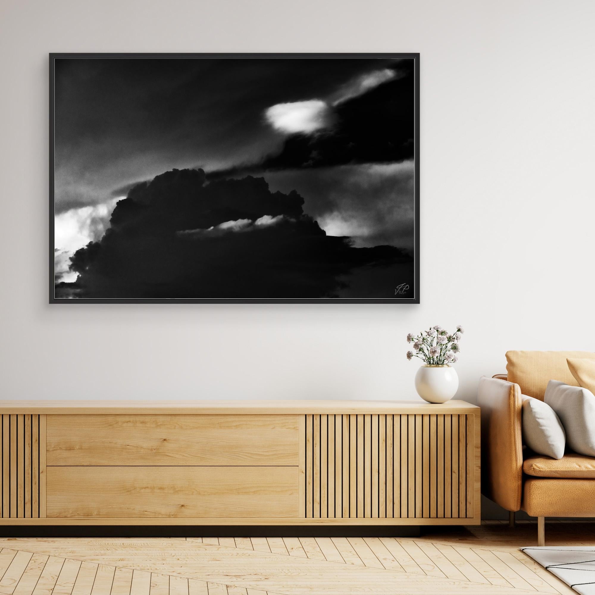 A modern living room with a wooden sideboard, artwork of dramatic clouds, and a small vase of flowers.